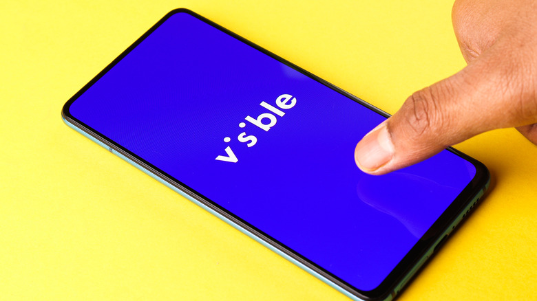 A finger touching a phone with the Visible logo on it.