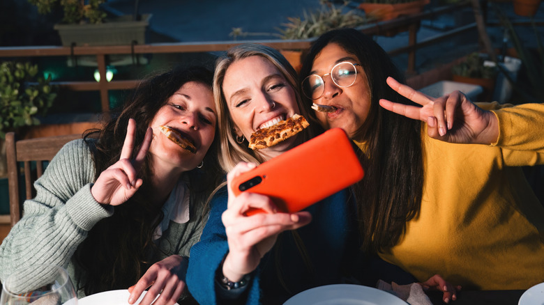 Three young girls taking a selfie with pizza in their mouths.